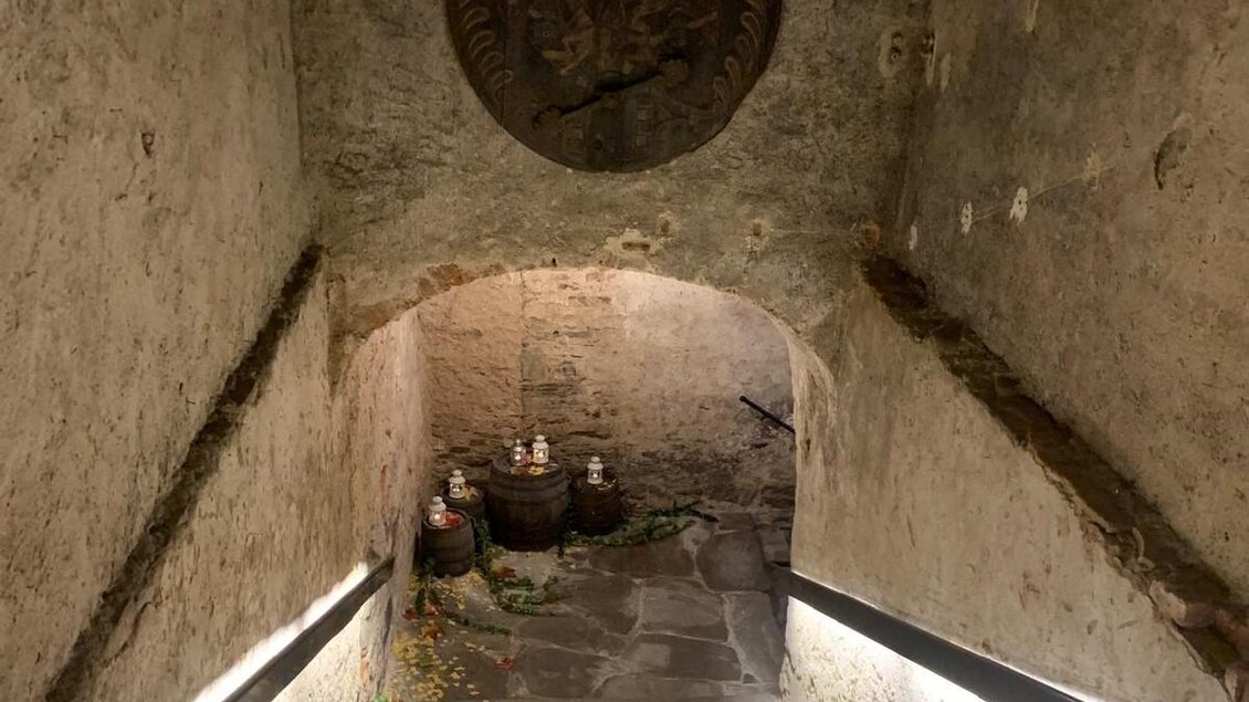 Eine alte Treppe führt in einen Keller mit steinernen Wänden. Am Ende der Treppe stehen Fässer und dekoratives Grün. | © TV Südsteiermark - Irene Löschnig