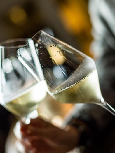 Two glasses of champagne clink together. Blurry lights can be seen in the background. | © TV Südsteiermark