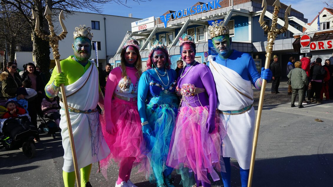 Fünf Personen in bunten Kostümen stehen auf einer Straße. Sie sind mit glitzernden Accessoires und farbiger Schminke geschmückt. | © Stadtgemeinde Köflach