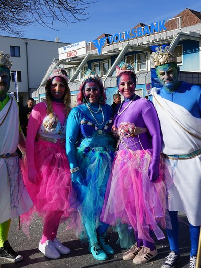 Fünf Personen in bunten Kostümen stehen auf einer Straße. Sie sind mit glitzernden Accessoires und farbiger Schminke geschmückt. | © Stadtgemeinde Köflach