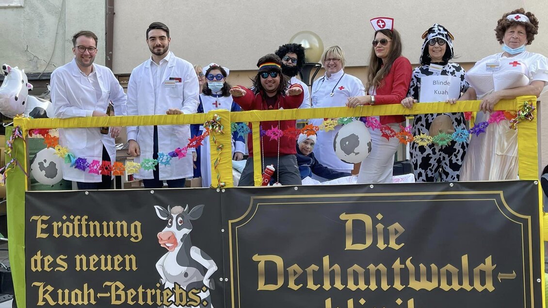 Eine Gruppe von Menschen steht auf einem Wagen, verkleidet als Ärzte und Krankenschwestern, mit einer Präsentation für die neue "Dechantwald-Klinik". Sie feiern das bevorstehende Ereignis mit bunten Kostümen und humorvollen Accessoires. | © Stadtgemeinde Köflach