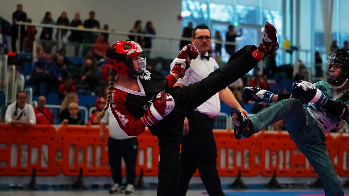 Ein Kampfturnier mit Kämpfern in speziellen Anzügen und Schutzausrüstung. Zuschauer beobachten das Geschehen im Hintergrund. | © Hütter