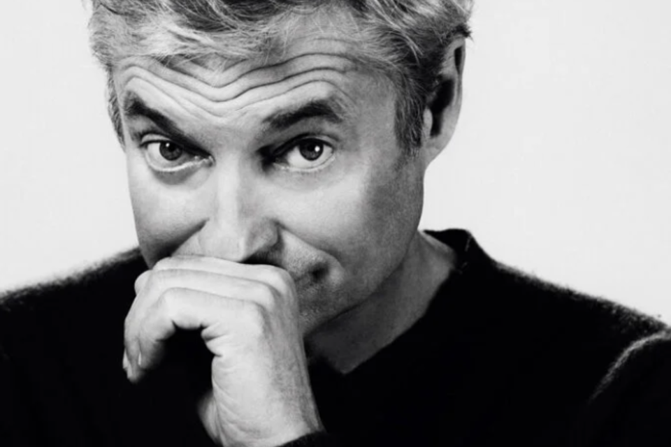 Ein Mann lächelt geheimnisvoll und hält seine Hand an das Gesicht. Im Hintergrund steht der Schriftzug "DORFER GLEICH" in großem, auffälligem Gelb. | © Alfred Dorfer