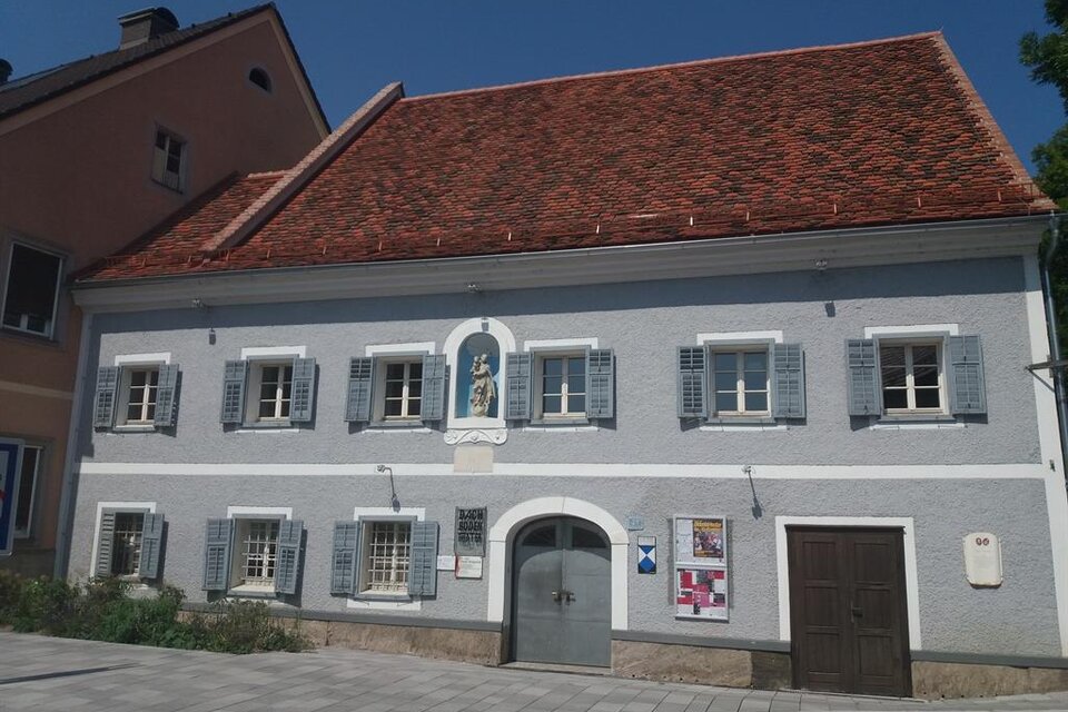 Ein historisches Gebäude mit grauer Fassade und roten Dachziegeln. Die Fenster sind mit blauen Läden versehen und es gibt eine Eingangstür in der Mitte. | © TV Südsteiermark - Irene Löschnig