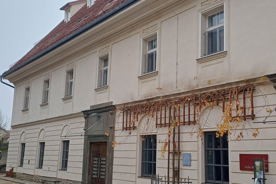 Ein historisches Gebäude mit hellen Wänden und einem Eingang aus Glas. Die Fassade ist von Weinreben umgeben, die im Herbst eine schöne Farbe haben. | © TV Südsteiermark - Irene Löschnig