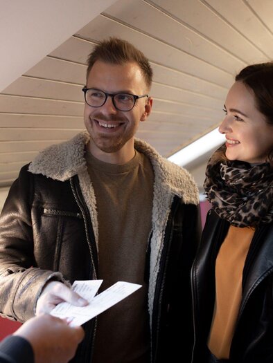 A couple is standing in a room and smiling. They are holding papers in their hands and seem to be making an agreement. | © TV Südsteiermark - Achromatic Photography