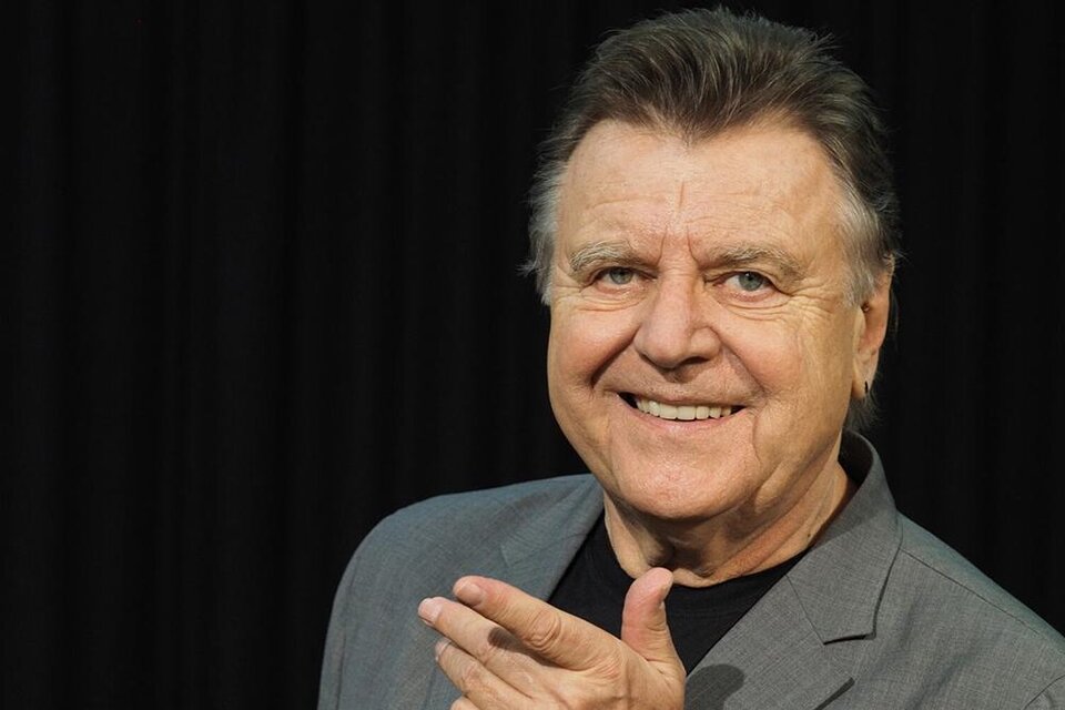 Ein lächelnder Mann in einem grauen Anzug, der mit einer Hand auf sich selbst zeigt. Der Hintergrund ist schwarz und sorgt für einen klaren Kontrast. | ©  Katrin Werzinger