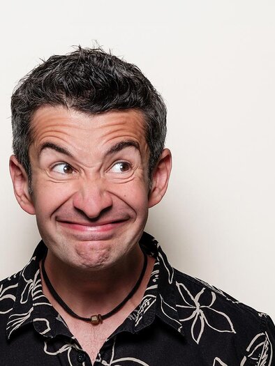 A man with a humorous expression is wearing a black Hawaiian shirt. The background is simple and bright. | © Stefan Gergely