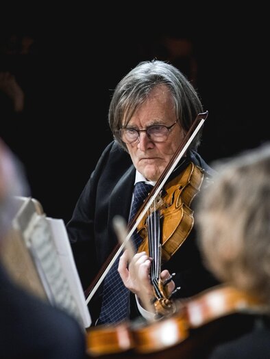 An older man is playing the violin on a stage. He is wearing a suit and is concentrating on the music. | © Ernst Friessnegg