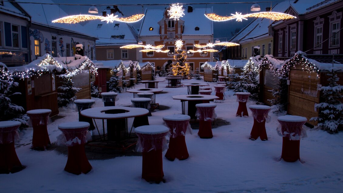 Ein festlich dekorierter Platz mit Schnee und beleuchteten Weihnachtssternen. Tische und Stühle sind für Besucher vorbereitet, um die winterliche Atmosphäre zu genießen. | © Stadtgemeinde Kapfenberg
