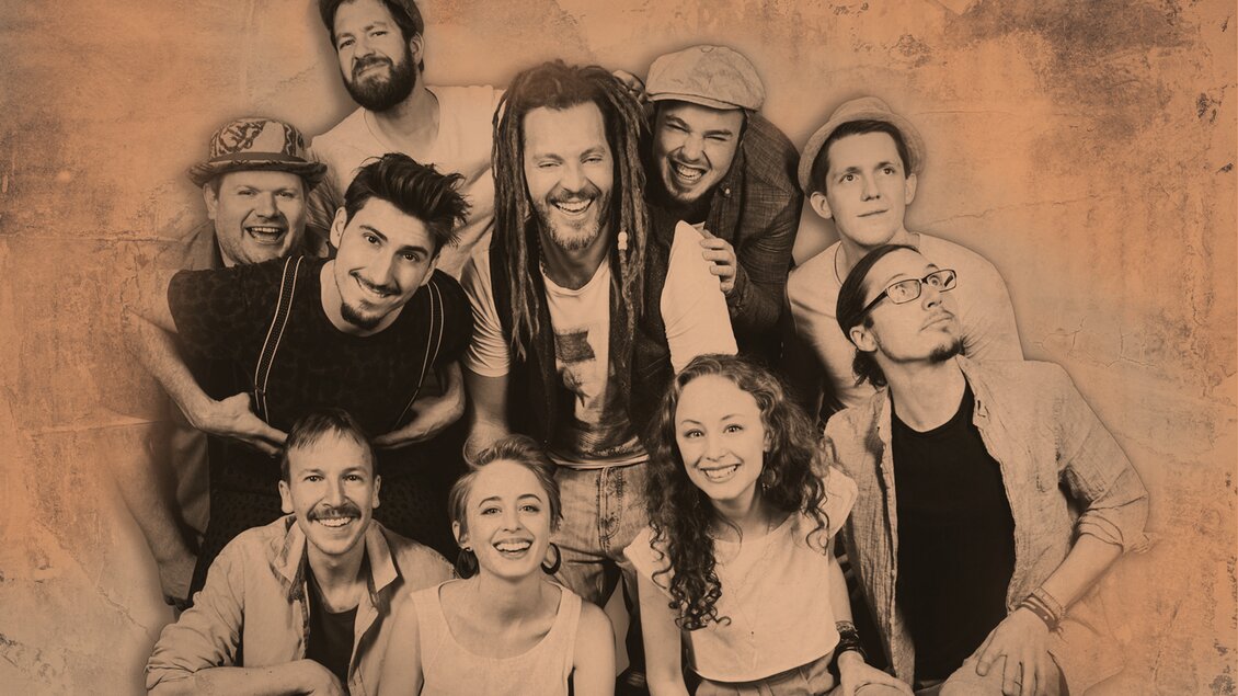 Eine Gruppe von neun Personen posiert gemeinsam vor einem neutralen Hintergrund. Sie haben unterschiedliche Stile und lachen freundlich in die Kamera. | © Meli Meisenpixel