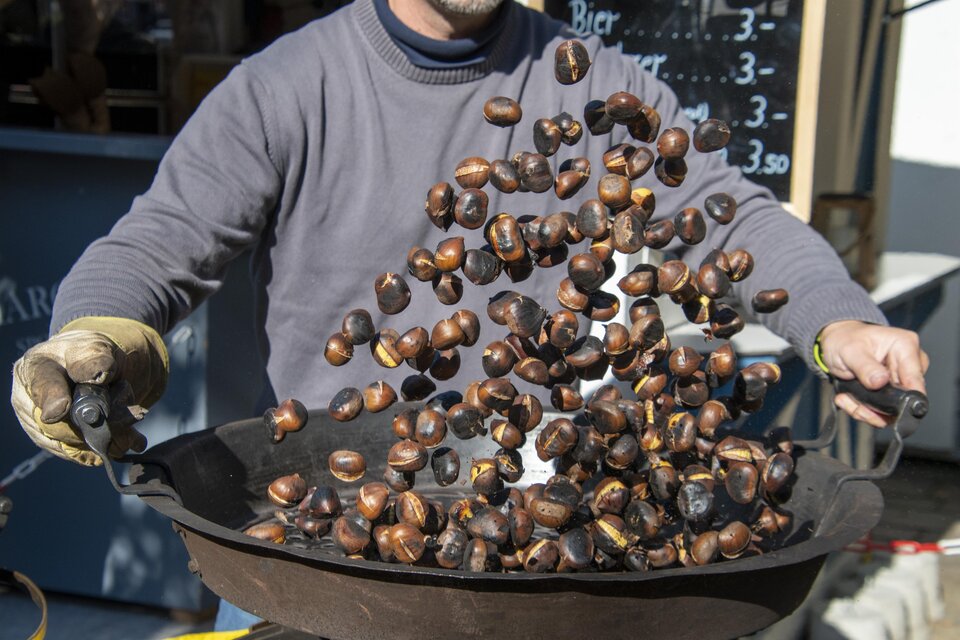 Ein Mann röstet Kastanien in einer großen Pfanne. Die Kastanien fliegen hoch und zeigen ein lebendiges Bild der Zubereitung. | © TVB Thermen- & Vulkanland