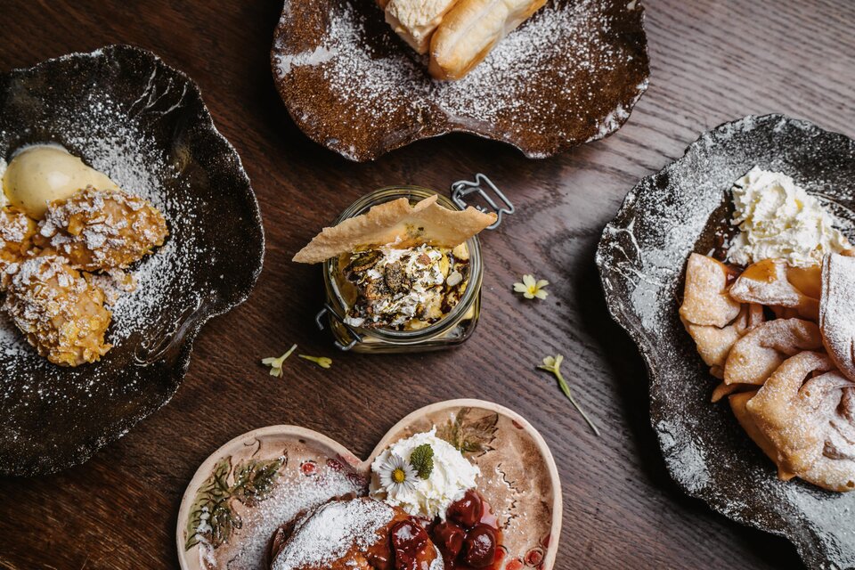 Eine Auswahl an köstlichen Desserts auf rustikalen Tellern. Die Leckereien sind dekoriert mit Puderzucker und frischen Zutaten. | © Michaela Lorber
