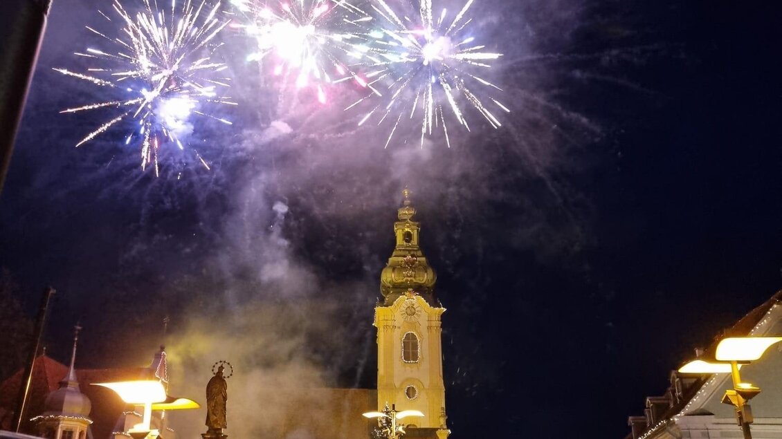 Ein festlicher Nachtmarkt mit vielen Menschen. Über der Stadt erleuchten bunte Feuerwerke den Himmel. | © Stadtmarketing Hartberg