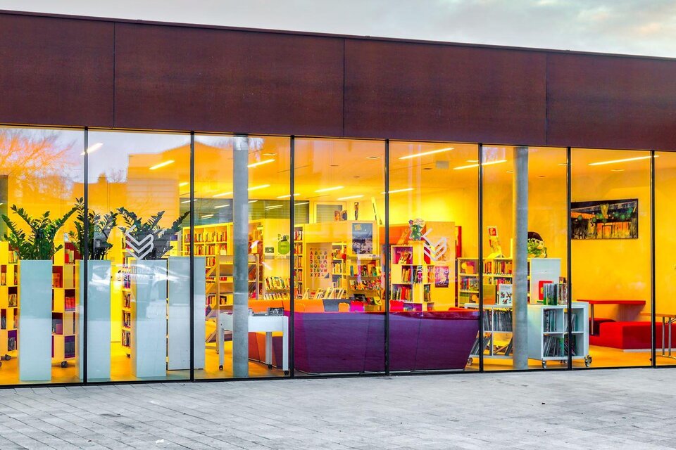 Ein modernes Gebäude mit großen Fenstern und einem einladenden Innenraum. Regale mit Büchern und gemütliche Sitzmöglichkeiten sind sichtbar. | © Petru Rimovetz