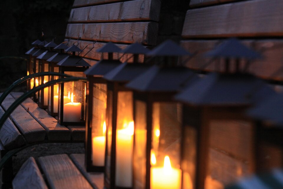 Eine Reihe von Laternen mit leuchtenden Kerzen steht auf einer Holzbank. Die warme Beleuchtung erzeugt eine gemütliche Atmosphäre in der Dämmerung. | © Thermen- & Vulkanland