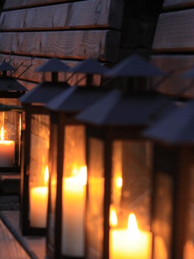 A row of lanterns with glowing candles is placed on a wooden bench. The warm lighting creates a cozy atmosphere in the twilight. | © Thermen- & Vulkanland