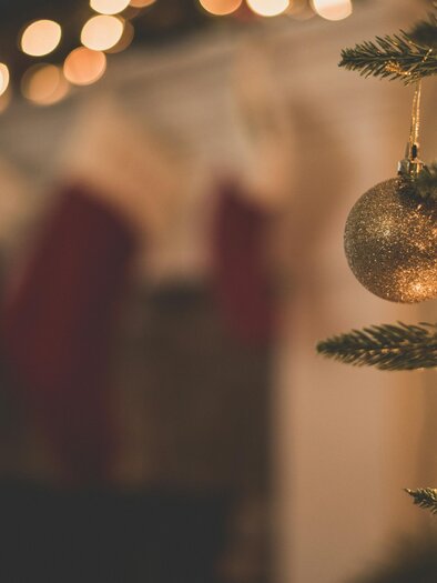 Ein Weihnachtsbaum mit einer glitzernden Christbaumkugel. Im Hintergrund hangen Weihnachtsstrümpfe und softes Licht schimmert. | ©  Unsplash@Chad Madden