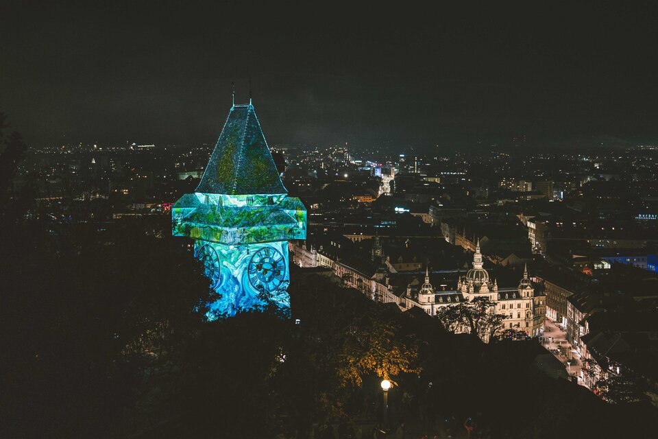 Ein beleuchteter Turm steht über der Stadt bei Nacht. Im Hintergrund sind die Lichter der Stadt zu sehen. | © © Luke_Goodlife for Klanglicht