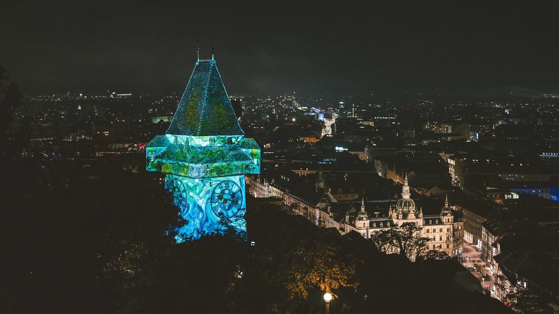 Ein beleuchteter Turm steht über der Stadt bei Nacht. Im Hintergrund sind die Lichter der Stadt zu sehen. | © © Luke_Goodlife for Klanglicht