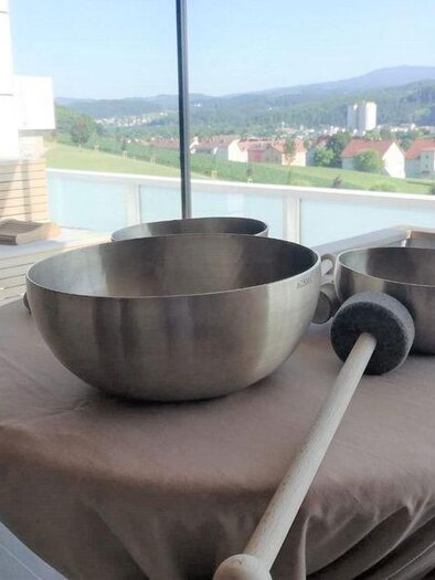 Three large metal bowls are standing on a table overlooking a green landscape. In the background, houses and mountains can be seen. | © Die Abbilderei