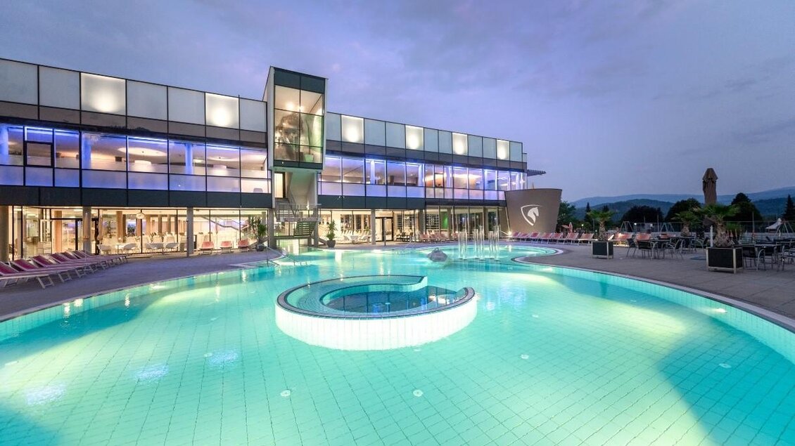 Ein modernes Hotel mit einem großen Pool. Der Pool hat eine runde Whirlpool-Ecke und ist bei Dämmerung beleuchtet. | © Lipizzanerheimat | Die Abbilderei