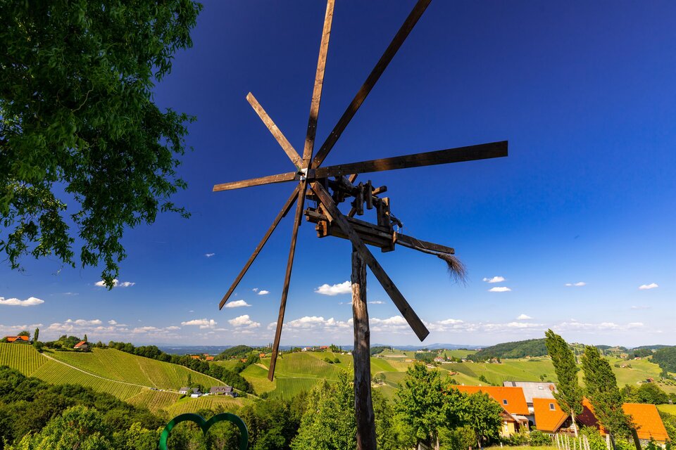 Eine alte Windmühle steht in einer grünen Landschaft mit sanften Hügeln. Der Himmel ist klar und blau, mit wenigen Wolken. | © TV Südsteiermark Harry Schiffer