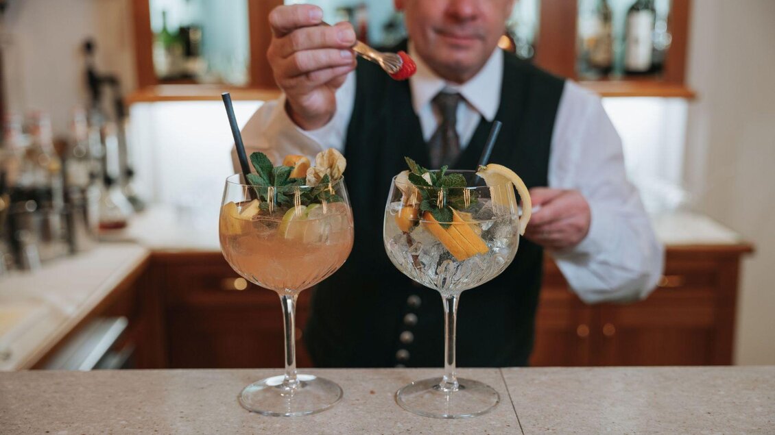 Ein Barkeeper bereitet zwei elegante Cocktails mit frischen Zutaten vor. Die Getränke sind in großen Gläsern serviert und dekoriert mit Minze und Zitrusfrüchten. | © Kalr Steinegger