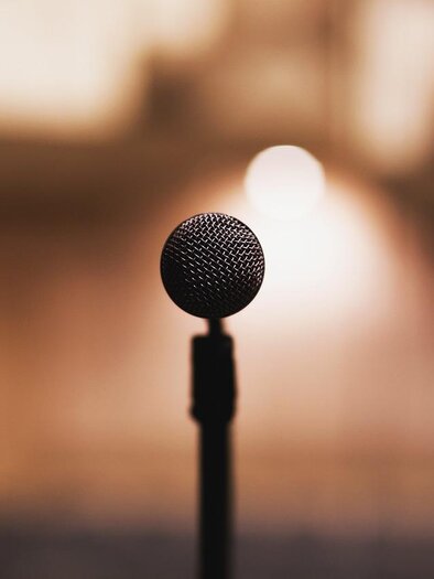 A microphone stands on a stand in front of a blurred background. It is ready for a presentation or performance. | © pixabay.com