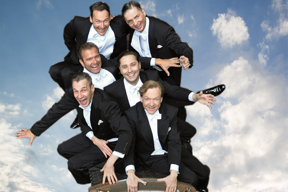 Eine Gruppe von sechs Männern in Abendanzügen posiert fröhlich auf einer Plattform. Der Himmel im Hintergrund ist blau mit einigen Wolken. | © Michael Bellmann