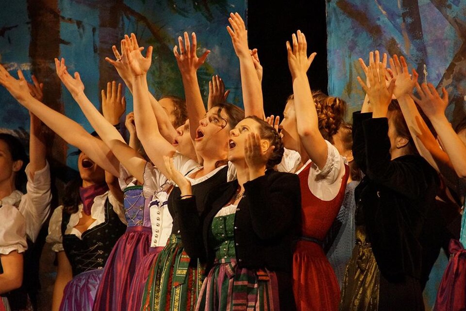 Eine Gruppe von Frauen in traditionellen Trachten singt begeistert auf einer Bühne. Ihre Hände sind erhoben und drücken Emotionen aus. | ©  Günter Pichler