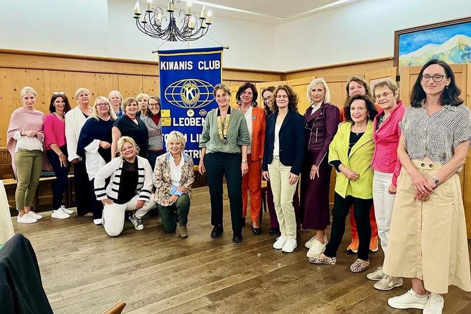 Eine Gruppe von Frauen versammelt sich in einem Raum vor einem Kinanis Club Banner. Sie tragen eine Vielzahl von bunten Outfits und lächeln freundlich in die Kamera. | ©  Kiwanis Club Leoben Forum Liuben