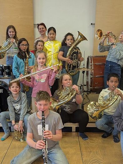 A group of children and teenagers is smiling with various musical instruments in a room. In the background, drums and other instruments are visible. | ©  Musik- und Kunstschule Leoben