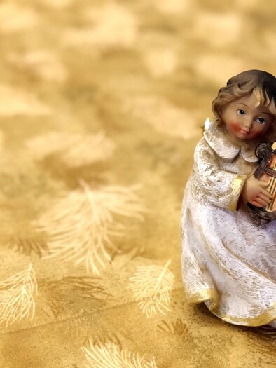 A small decorative figure of an angel playing a harp. It sits against a golden background with a soft texture. | © pixabay.com