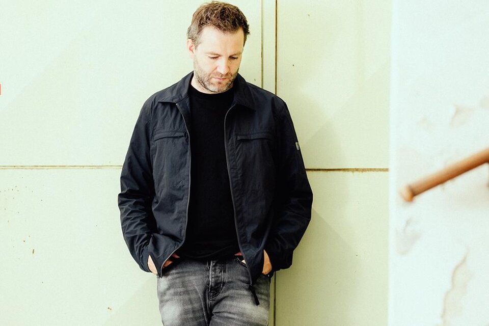 Ein Mann in einer dunkelblauen Jacke steht entspannt gegen eine helle Wand. Er schaut nach unten und trägt eine schwarze T-Shirt und Jeans. | ©  Philipp Hirtenlehner