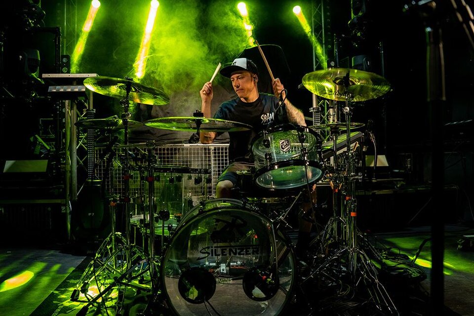 Ein Schlagzeuger spielt leidenschaftlich auf seiner Trommel. Helles Licht und Nebel schaffen eine energiegeladene Atmosphäre. | ©  Silenzer