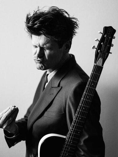 Ein Mann im Anzug hält eine Gitarre und schaut nachdenklich. Er scheint einen Moment der Inspiration zu erleben. | © (c) Georg Buxhofer