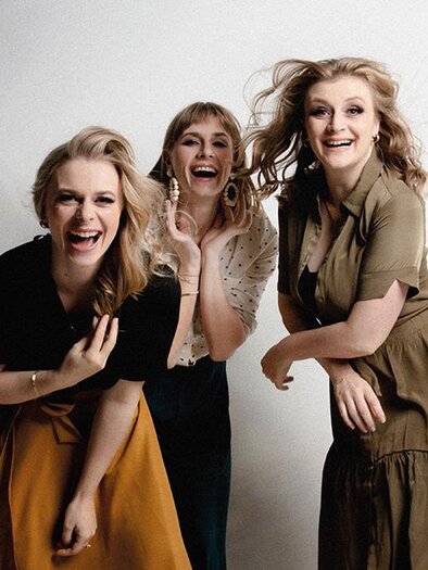Three women are smiling happily and posing in front of a neutral background. They are wearing different clothing and seem to be having a lot of fun. | ©  Zoe Goldstein Fotografie