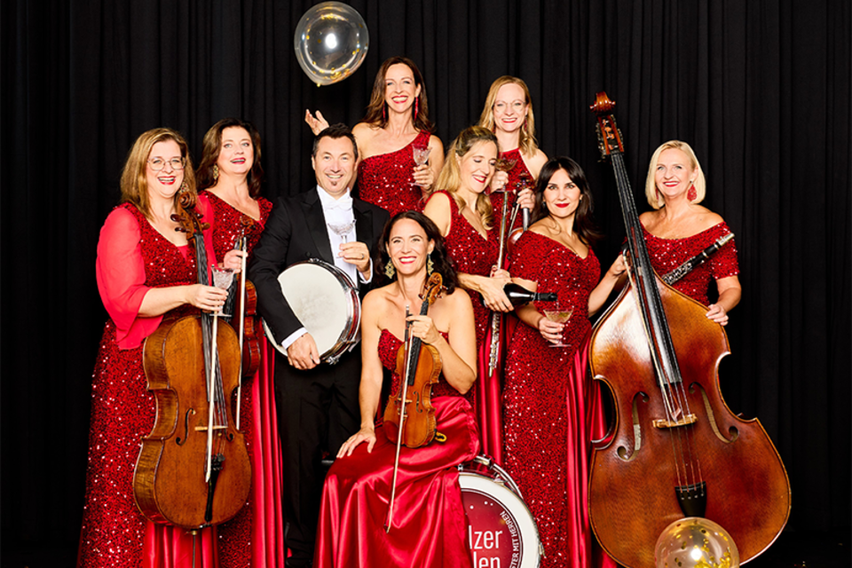 Eine Gruppe von Musikerinnen und Musikern in glitzernden roten Kleidern steht zusammen. Sie halten Instrumente und wirken festlich und elegant. | ©  Kurt Remling