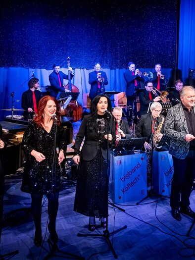 A lively music performance with several singers and a large band in the background. The artists are elegantly dressed and radiate energy. | © Kulturausschuss der Marktgemeinde Lannach
