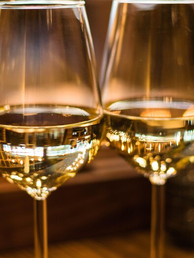 Zwei Glas Weißwein stehen auf einem Tisch. Das Licht reflektiert schön in den Gläsern. | © TV Südsteiermark