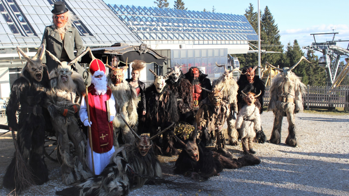 Eine Gruppe von Menschen in aufregenden und gruseligen Kostümen steht draußen zusammen. Im Vordergrund sieht man einen Weihnachtsmann und viele Kreaturen mit Tiermasken. | © @ St.Radegunder Schöcklpass