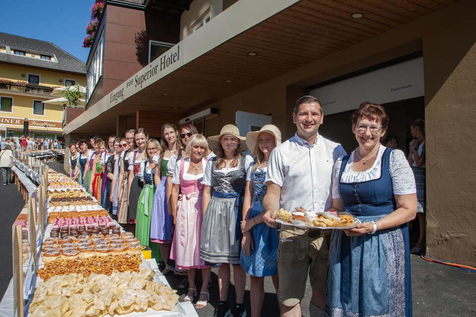 Eine Gruppe von Menschen in traditionellen Trachten steht vor einem festlich gedeckten Tisch mit verschiedenen Backwaren. Die Atmosphäre ist freundlich und einladend. | © Tourismusverein Mönichwald