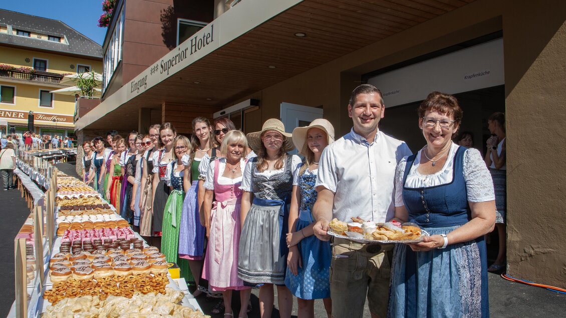 Eine Gruppe von Menschen in traditionellen Trachten steht vor einem festlich gedeckten Tisch mit verschiedenen Backwaren. Die Atmosphäre ist freundlich und einladend. | © Tourismusverein Mönichwald