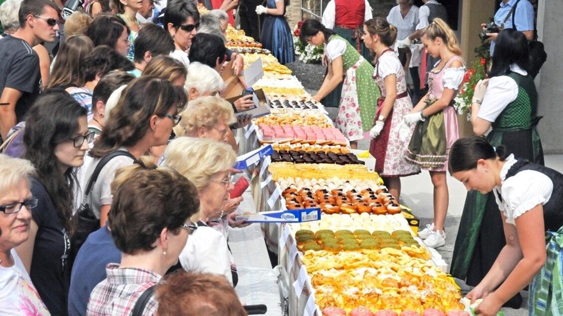 Eine bunte Auswahl von Desserts wird auf einem Tisch präsentiert. Viele Menschen schauen interessiert zu und einige tragen traditionelle Trachten. | © Oststeiermark Tourismus