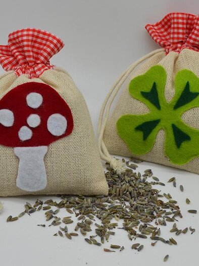 Two small fabric bags with different designs. One depicts a mushroom and the other a clover, surrounded by dried lavender. | © KulturQuartier