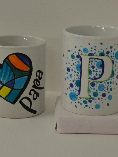 Zwei Tassen sind auf einem Tisch platziert. Die linke Tasse hat ein buntes Herzdesign, während die rechte Tasse mit blauen Punkten und einem großen Buchstaben "P" verziert ist. | ©  KulturQuartier Leoben