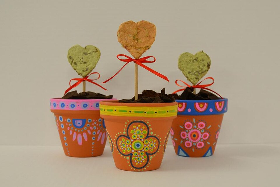 Drei bunte Blumentöpfe mit dekorativen Herzen auf Stäben stehen auf einem Tisch. Jeder Topf ist einzigartig bemalt und mit Erde gefüllt. | ©  KulturQuartier Leoben