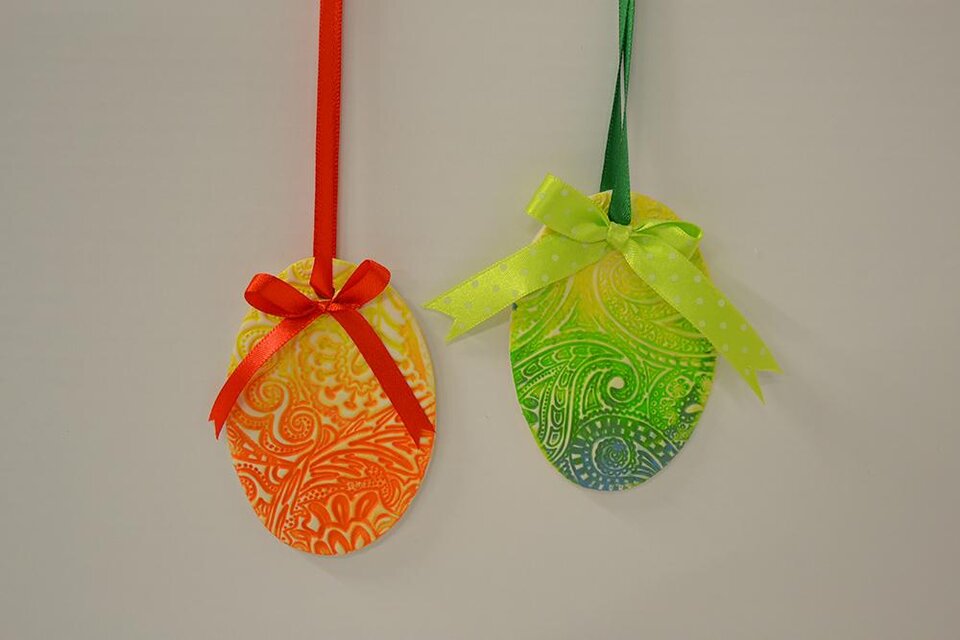 Zwei farbenfrohe Ostereier hängen an Bändern. Das orangefarbene Ei hat ein rotes Band, das grüne Ei ein grünes mit Punkten. | © KulturQuartier Leoben