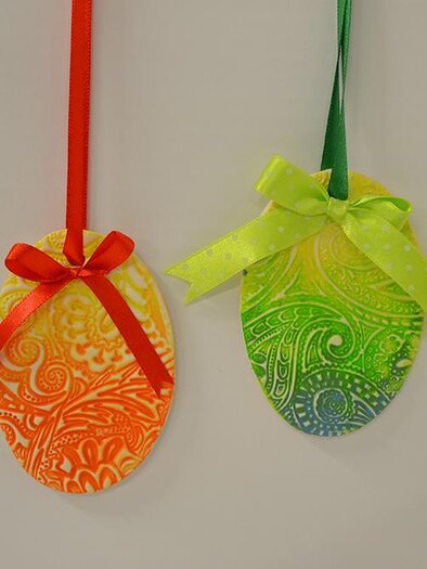 Two colorful Easter eggs hang from ribbons. The orange egg has a red ribbon, the green egg has a green one with polka dots. | © KulturQuartier Leoben